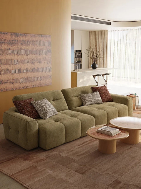 Olive linen CloudNest sofa beneath abstract artwork with honey-toned walls and round stone tables. Digital interior design study.