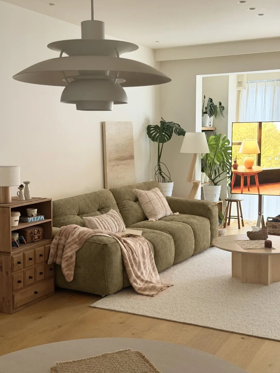 Olive CloudNest sofa with a patterned throw, pale rug, timber cabinet and sculptural pendant in a warm Scandinavian-inspired room. Digital sofa styling study.